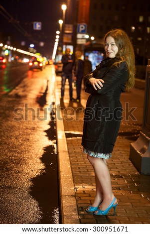 Pretty frozen woman in black coat and high heels walking alone on the pavement in the night city