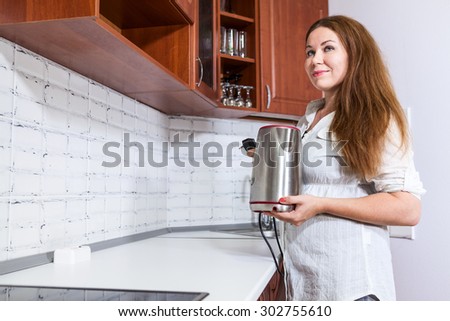 Thoughtful dreaming housewife with steel electric tea kettle in hands, domestic kitchen, copy space