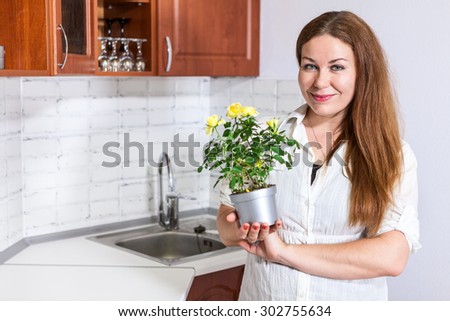 Woman housewife holding yellow roses at pot in hands, kitchen, copy space