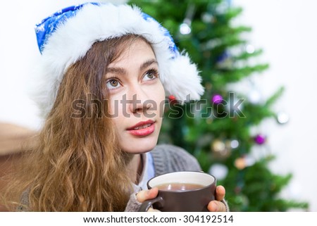 Attractive woman in blue Santa hat holding hot tea mug in hands