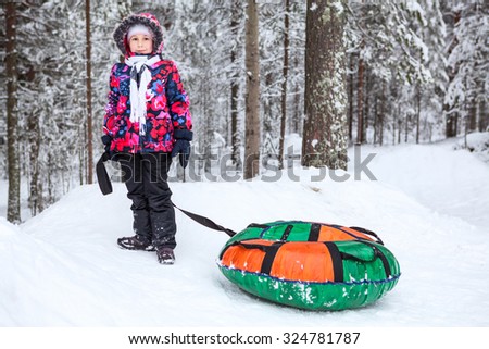 Pretty girl in warm clothes standing with tube for winter slope riding. Snowy forest