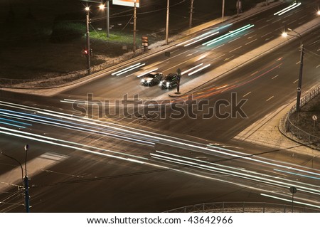 Two cars at a crossroads wait at night a green signal of a traffic light. Night shooting. Bright traces of headlights of cars