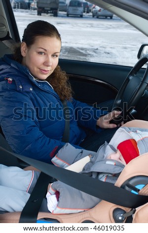 The child in a safety seat near to mother who sits on forward sitting of the car. Child not in focus