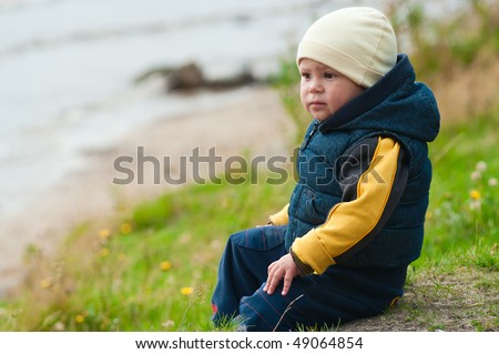 Young boy sitting on the rocks next to a lake lonely. He is in melancholy mood