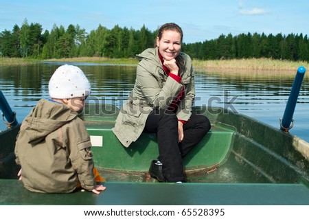 Mother and son together ride in a rowboat on a lake in woodland. Unrecognizable child not in focus