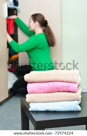 Stack of clothes and young caucasian woman arranging things in the wardrobe on background.
