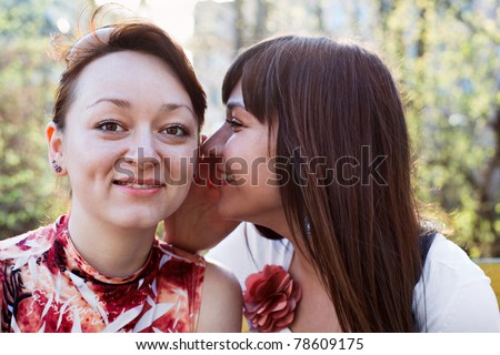 Young beautiful woman whispers something to girlfriend in her ear