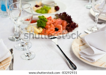 Plates with cold snack on table, cutlery for dinner, white napkin, selective focus.