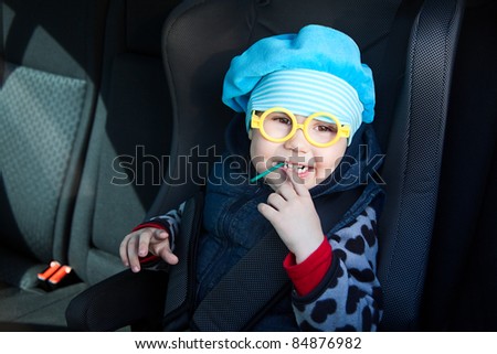 Little child sitting in carseat in vehicle with lollipop. Funny glasses