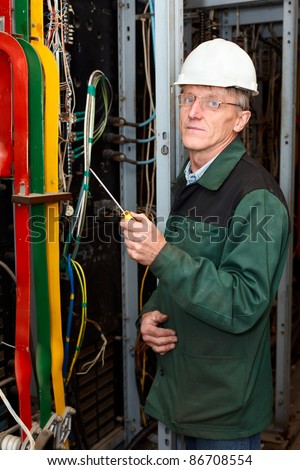 Mature electrician worker in hard hat with screwdriver is in an industrial plant