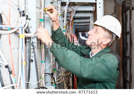 Senior electrician worker inspecting high voltage box in hard hat with screwdriver