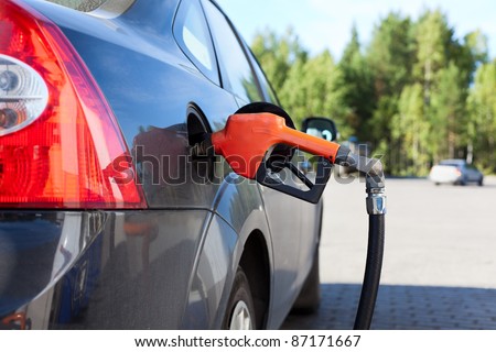 Refueling nozzle in the tank black car at fuel filling column. Summer day. Black car