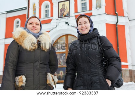 Two Russian women in winter clothes against Orthodox monastery building. Pilgrimage