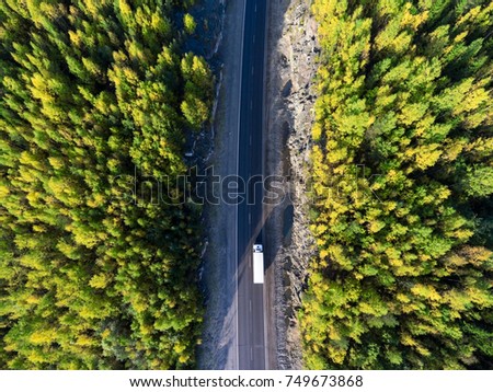 Top view at white freight truck driving between rock tunnel in golden autumn forest of Karelia, Russia