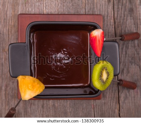Chocolate fondue with fresh fruits on wood