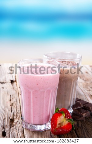 Fresh milk, strawberry and chocolate drinks on wodeen table, assorted protein cocktails with fresh fruits. Summer drinks on the beach with blue sky.