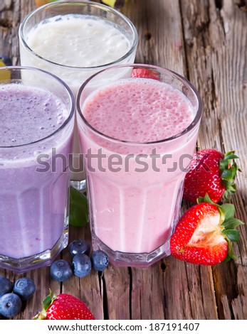 Fresh milk shake on wooden table. Three milk drinks, blueberry, strawberry and banana with fruits.