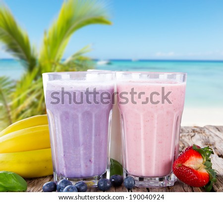 Fresh milk, strawberry and blueberry drinks on wodeen table with tropical beach, assorted protein cocktails, fruits.