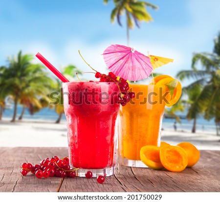 Fresh currant and apricot juice on wooden table with tropical beach background. Summer drink, concept.
