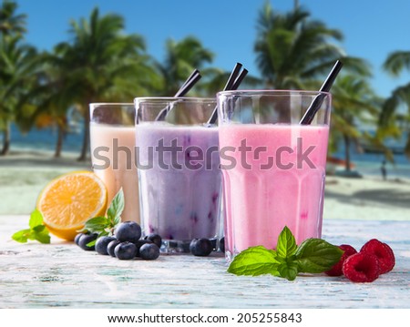 Fresh milk, strawberry, blueberry and banana on wooden table, assorted protein cocktails with fresh fruits. Natural background. Tropical beach.