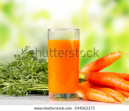 carrot juice and carrot segments on a wooden background with nature green background.