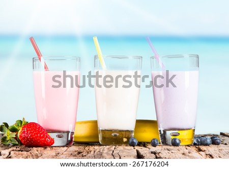 Fresh milk, strawberry, blueberry and banana drinks on wooden table, assorted protein cocktails with fresh fruits. Tropical beach background