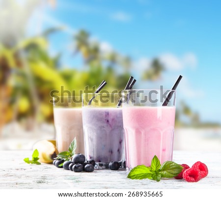 Fresh milk, raspberry, banana and blueberry drinks on wooden table, assorted protein cocktails with fresh fruits. Natural background. Tropical beach, sea, summer concept.