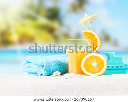 Fresh orange juice, fruits and children cake on sand with blue sky background, summer concept