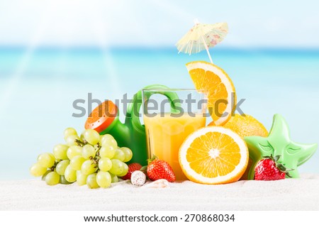 Fresh orange juice, fruits and children cake on sand with blue sky background, summer concept