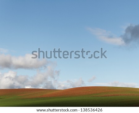 Hill farmland with light-weight clouds.