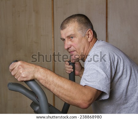 Muscular adult man is training by exercise bike.