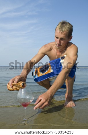 Young man relax on the beach, he filling the cup of wine.