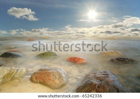 Wonderland with stones in water and sun on the sky.