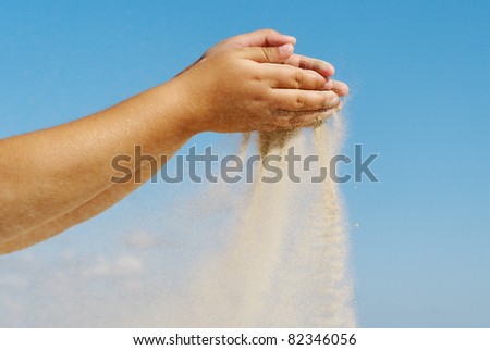 Sand is pouring out from a girl hands on sky background.