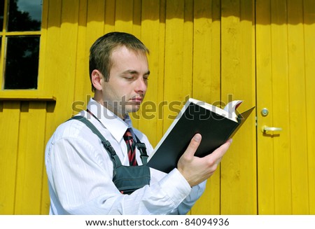 Young man wear jumpers outside and read black book.