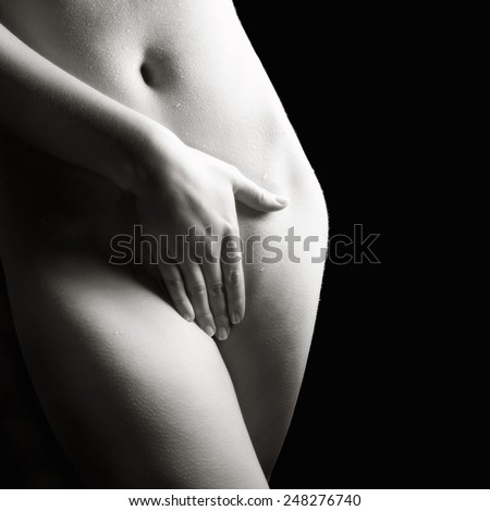 Monochrome closeup of a beautiful nude woman covering herself with her hand in front of black studio background