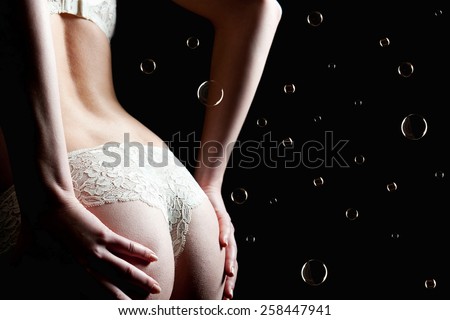 Beautiful back of a woman wearing white panties and bra in front of dark studio  background, photo with copy space and soap bubbles on the right side of the image