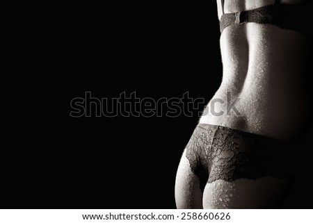 Beautiful back of a woman wearing undies and bra in front of black studio background, monochrome closeup photo with copy space on the left side of the image