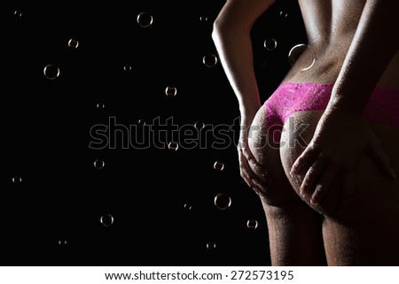 Beautiful back of a woman wearing pink panties in front of dark studio background, photo with copy space and soap bubbles on the left side of the image