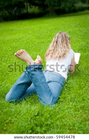 Beautiful young curly blond woman reading a book in a park