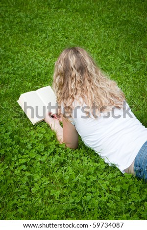 Beautiful young curly blond woman reading a book in a park