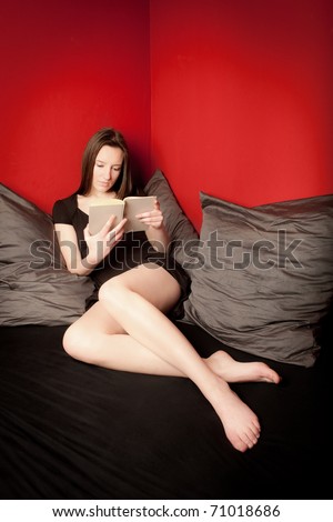 Pretty young woman reading a book in front of red wall