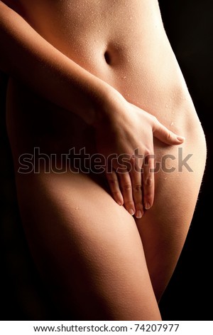 Beautiful naked woman covering herself with her hand in front of black background