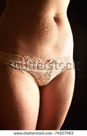 Wet body of a sexy young female in beautiful white panties in front of black background