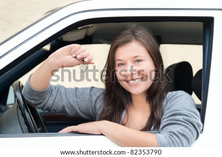 Young woman sitting in car and showing key. She is happy about her new drivers license or new car