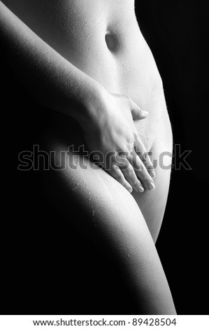 Beautiful naked woman covering herself with her hand in front of black background, black and white photo