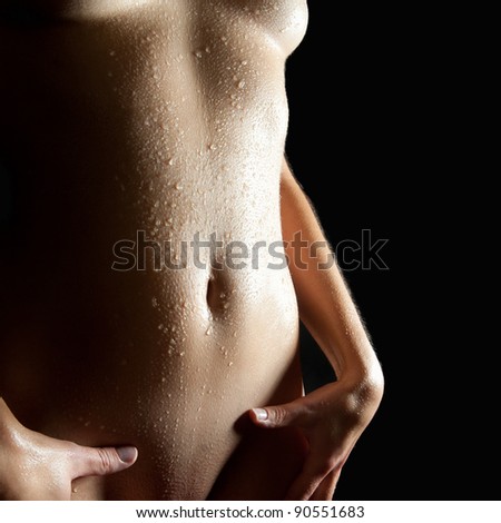 Closeup of a slim wet body of a beautiful nude young woman in front of black background