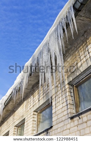 Very cold in winter concept. Huge icicles hanging on roof of a brick old rustic building on a background of frozen blue sky. Sunny december day