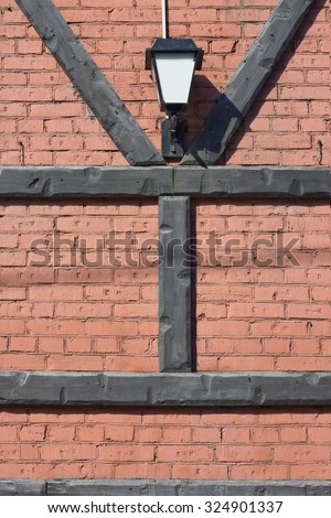 The lantern  hangs on a red  brick wall. Wooden pine logs are laid in the form of Y and H of letters. Concept of secret. Sunny day