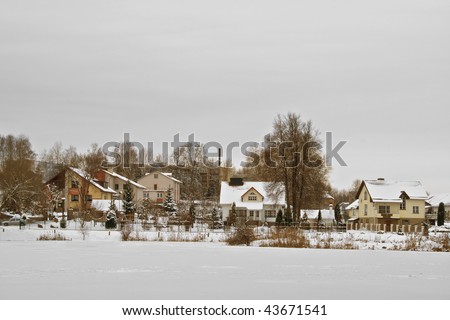 Some the beautiful, rural houses brought by fresh snow stand on the bank of the stood lake. Cloudy day.